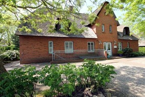 A brick building with a pitched roof, a gated entrance, and a small garden area with shrubs. - But Dörp 3, Holiday Apartment 3 (Wyk auf Föhr)
