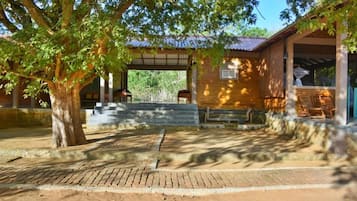 A covered outdoor area with a brick building, a large tree, and a paved walkway.