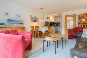 Ein Wohnzimmer mit einem roten Sofa, einem grauen Sofa und einem Essbereich mit Holztischen und einer Tischplatte.