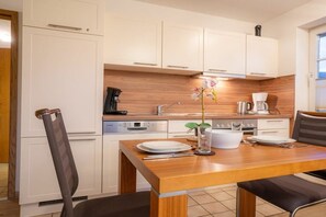A compact kitchen with white cabinets, a wooden countertop, and a dining area with a table set for two. - 6 in the Pole Poppenspäler house (ID 211) (St. Peter-Ording)