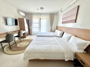 Una habitación de hotel con cama, escritorio, silla, televisor y un ventanal con cortinas.