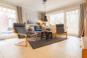 Ein modernes Wohnzimmer mit einer Couch, zwei Sesseln, einem Couchtisch und einer Pendelleuchte.