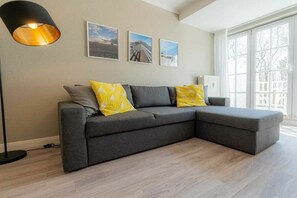 Ein modernes Wohnzimmer mit einem grauen Ecksofa, einer Stehlampe und drei gerahmten Bildern an der Wand.