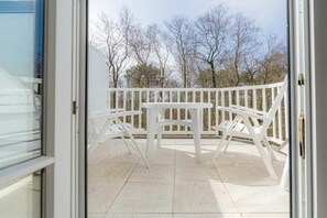 Eine Terrasse im Freien mit einem weißen Tisch und Stühlen, einem weißen Zaun und Bäumen im Hintergrund.