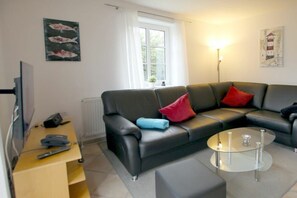 Ein modernes Wohnzimmer mit einer Ledersofa, einem Glastisch und einem Flachbildfernseher auf einem Standfuß.
