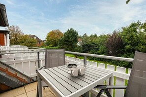A balcony with a table and chairs, a white fence, and greenery in the background. - 10 in the Nis Randers house (ID 291) (St. Peter-Ording)