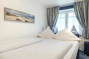 Ein Hotelzimmer mit Bett, einem Fenster mit Vorhängen und einem Gemälde an der Wand.