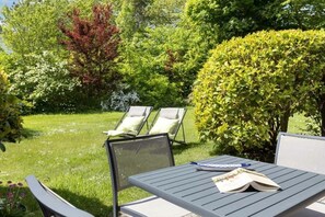 Eine Terrasse mit Tisch und Stühlen, umgeben von üppiger Bepflanzung und Bäumen.