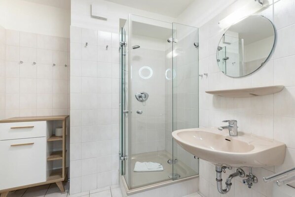 Un baño moderno con ducha envuelta en vidrio, un lavabo blanco y un espejo redondo.