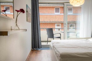 A hotel room with a bed, a chair, a window with curtains, and a view of a brick building. - Holiday apartment with 2 bedrooms (St. Peter-Ording)