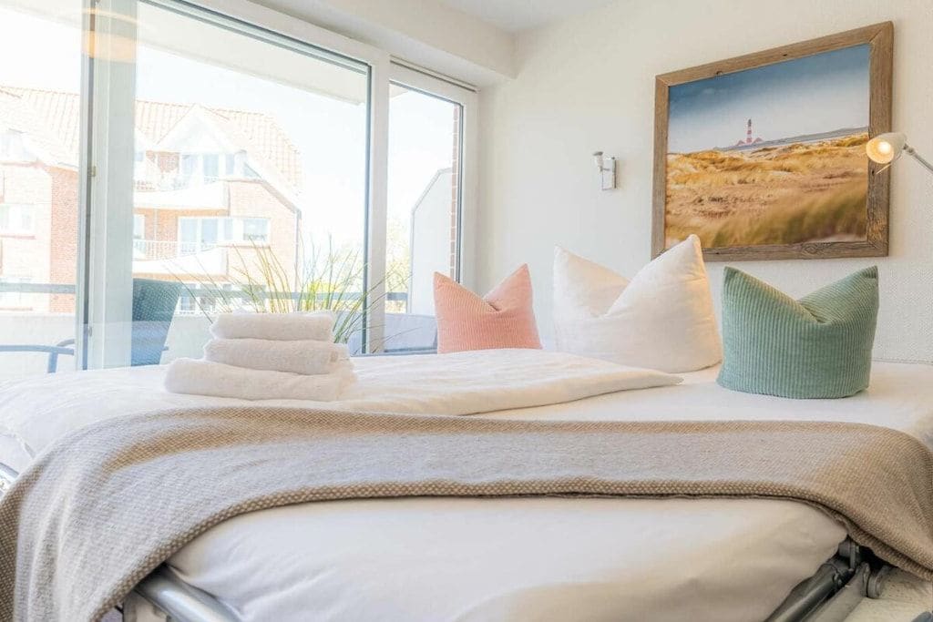Een hotelkamer met een bed, kussens, een inlijsting foto aan de muur en een raam met uitzicht op gebouwen.