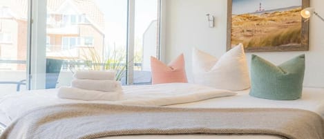 Habitación de hotel con cama, almohadas, un cuadro enmarcado en la pared y una ventana con vista a edificios.