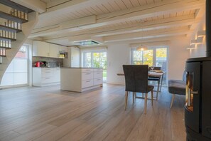 A modern kitchen with white cabinets, a dining area with a table and chairs, and a wood-burning stove. - Dat Lütte Huus (ID 424) (Tümlauer Koog)