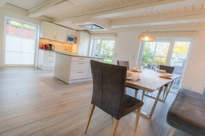 A modern kitchen with white cabinets, a central island, and a dining area with a table and chairs. - Dat Lütte Huus (ID 424) (Tümlauer Koog)