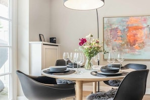 A dining area with a round table set for four, black chairs, a vase with flowers, and a large abstract painting on the wall. - Holiday home Captain Karl Keitum / Sylt (Nordfriesland)