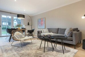 A modern living room with a grey sofa, a round coffee table, and a wicker chair. - Holiday home Captain Karl Keitum / Sylt (Nordfriesland)