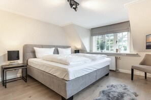 A bedroom with a bed, bedside tables, a window with a view, and a chair. - Holiday home with 1 bedroom (Nordfriesland)