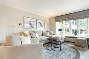 A modern living room with a sectional sofa, a round coffee table, and a large window with a view of greenery. - Holiday home with 1 bedroom (Nordfriesland)