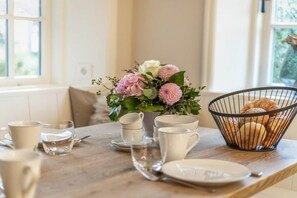 A dining table with a floral centerpiece, a basket of bread, and a window with a view of greenery. - Holiday home with 1 bedroom (Nordfriesland)