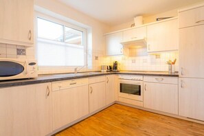 A kitchen with white cabinets, a microwave, a stove, and a window. - House section 30 "Sea Lavender" (ID 461) (St. Peter-Dorf)