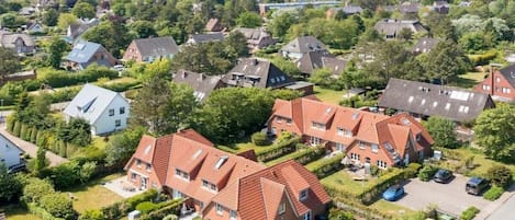 A residential area with houses, some with sloped roofs and others with flat roofs, surrounded by greenery and a clear sky.