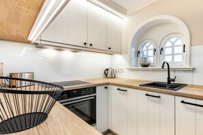 A modern kitchen with white cabinets, a black countertop, and a window with arched design. - Holiday home with 1 bedroom (Nordfriesland)
