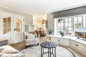 A spacious living area with a sofa, a round table, and a view of the outdoors through large windows. - Holiday home with 1 bedroom (Nordfriesland)