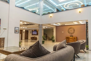 Een moderne lobby met glazen dak, een receptiebalie en een zithoek met banken.