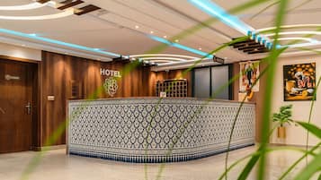A hotel reception area with a patterned reception desk, a reception sign, and a wall-mounted security camera.
