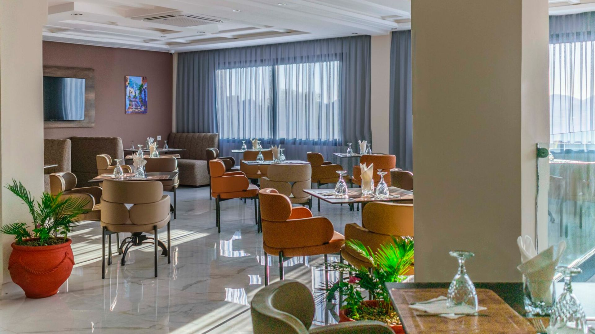 Un vestíbulo de hotel con varias zonas de estar, incluyendo sofás y mesas, y un ventanal con cortinas.