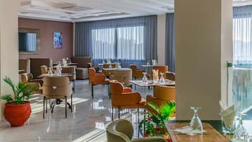 Un vestíbulo de hotel con varias zonas de estar, incluyendo sofás y mesas, y un ventanal con cortinas.