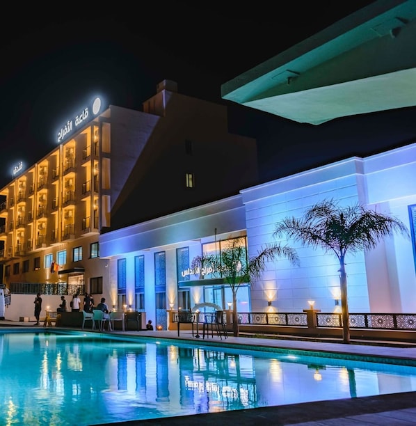 A hotel with a swimming pool, outdoor seating, and a well-lit facade.