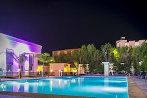 Una piscina con sillones de descanso y una estatua, rodeada de edificios y follaje.