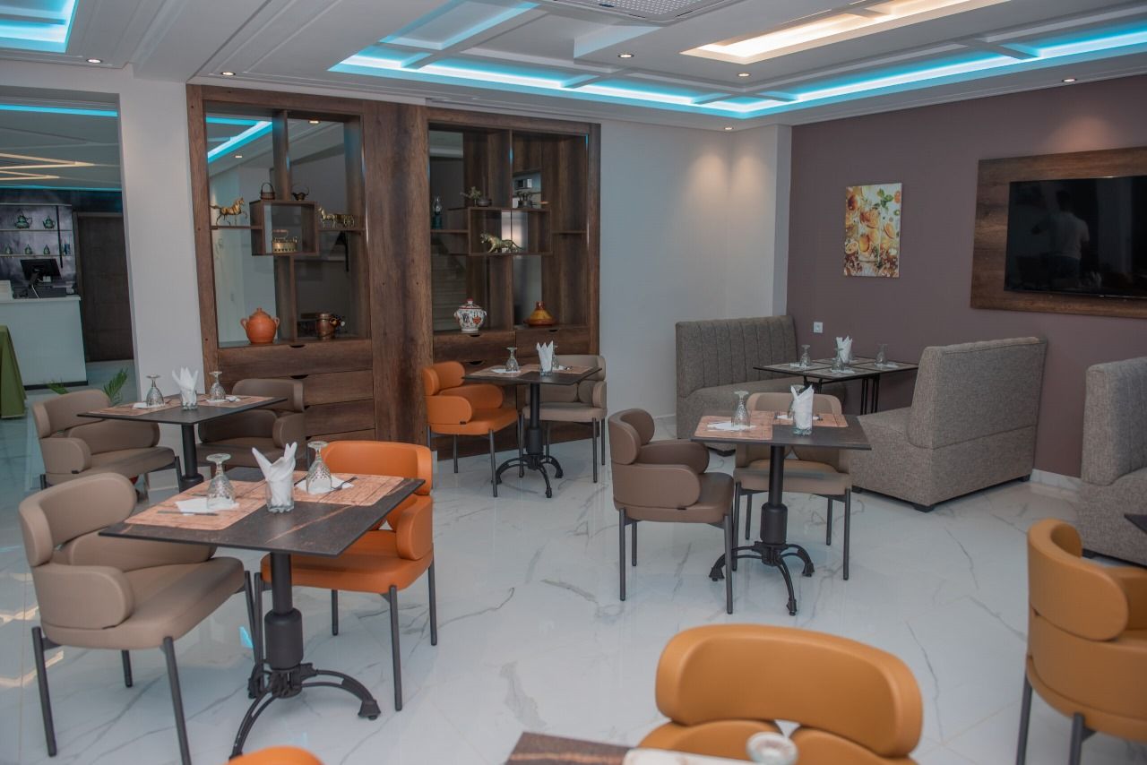 Interior moderno de restaurante con varias zonas de estar, incluyendo mesas y sillas, y una barra visible a través de un tabique de madera.
