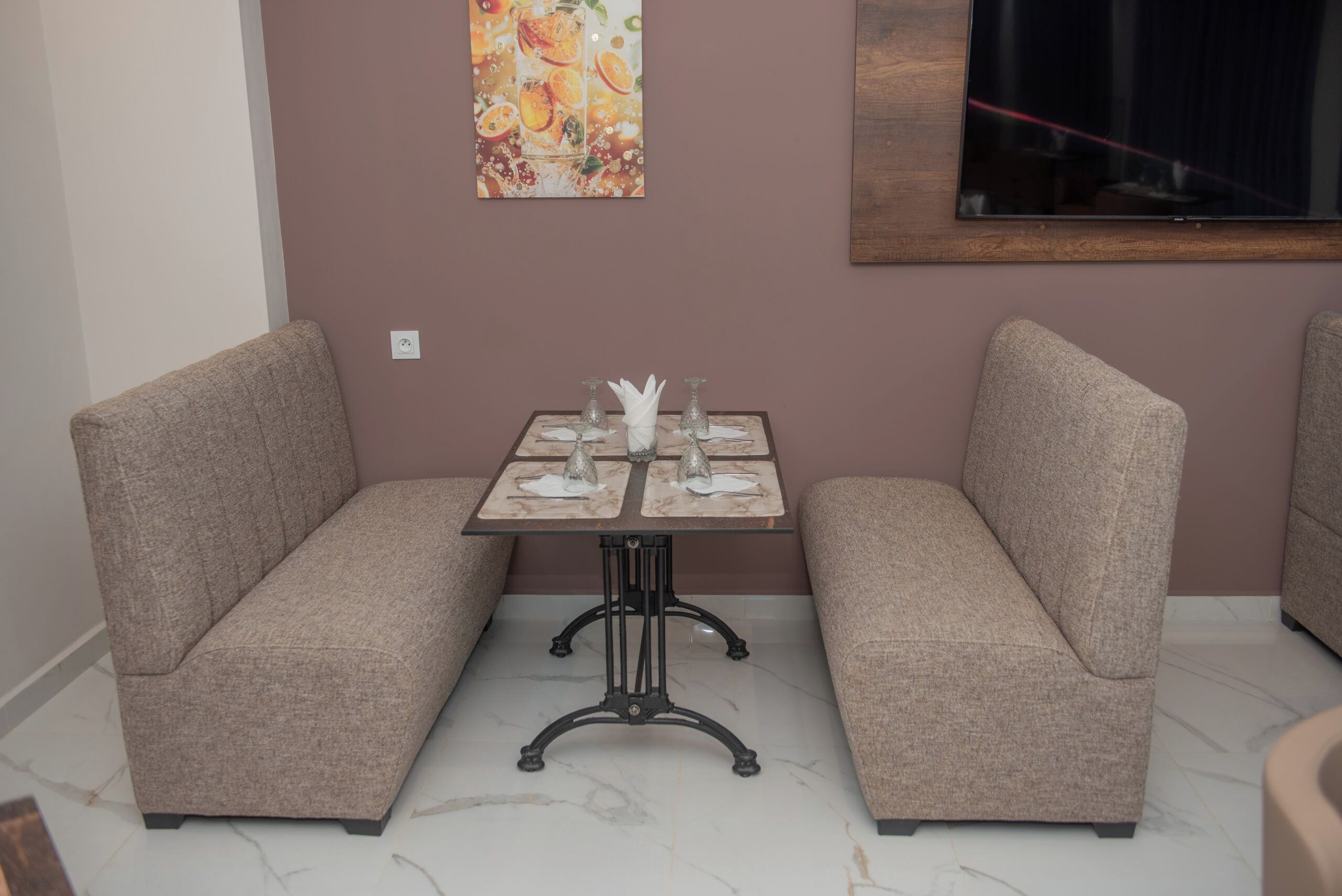 A corner seating area with two cushioned sofas, a small table with a glass top, and a wall-mounted painting.