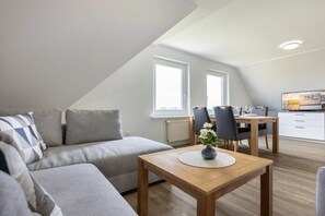 A modern living room with a sofa, a dining table with chairs, and a kitchen area in the background. - OG in the Everschop house (ID 135) (St. Peter-Ording)