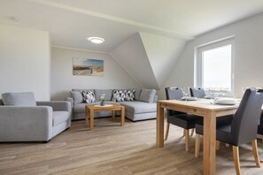 A modern living room with a sofa, a dining table with chairs, a small coffee table, and a painting on the wall. - OG in the Everschop house (ID 135) (St. Peter-Ording)