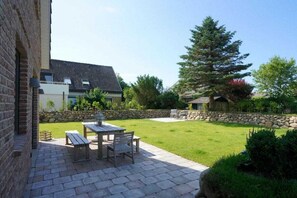 Eine Terrasse mit Tisch und Stühlen, eine Steinmauer und eine Rasenfläche.
