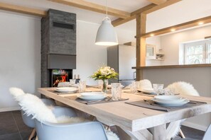 A dining area with a long wooden table set for four, a modern pendant light, and a fireplace in the background. - "Vörn Binnendiek" (ID 376) (St. Peter-Bad)