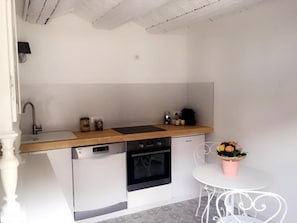 A compact kitchen with a dishwasher, oven, and a small sink. There's a round table with a vase of flowers.