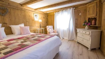 Een kamer met houten vloeren, een bed, een stoel, een dressoir en een raam met gordijnen.