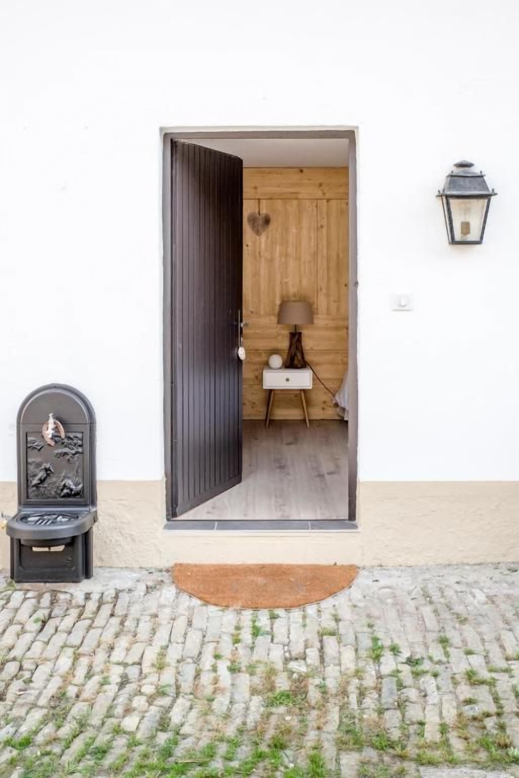 Een deuropening naar een kamer met een houten inrichting, een klein tafeltje met een lamp en een wandlamp.