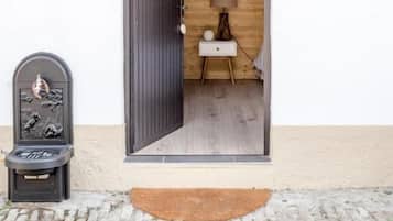 Een deuropening naar een kamer met een houten inrichting, een klein tafeltje met een lamp en een wandlamp.