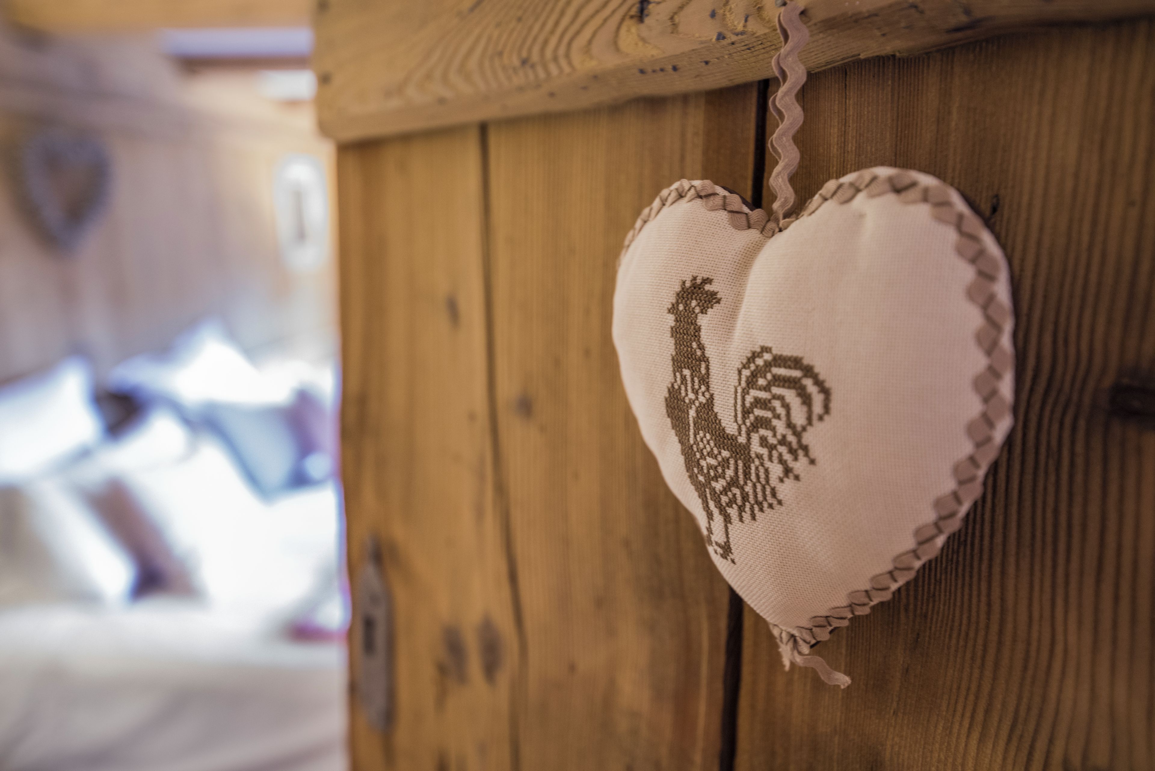 Un objeto con forma de corazón, bordado con un diseño de gallo, colgado en una pared de madera.