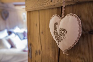 A heart-shaped embroidered item with a rooster design hanging on a wooden wall.