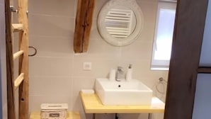 A bathroom with a wooden beam ceiling, a white sink, a mirror, and a window. - LA GRANGE AUX COQS (Ittenheim)