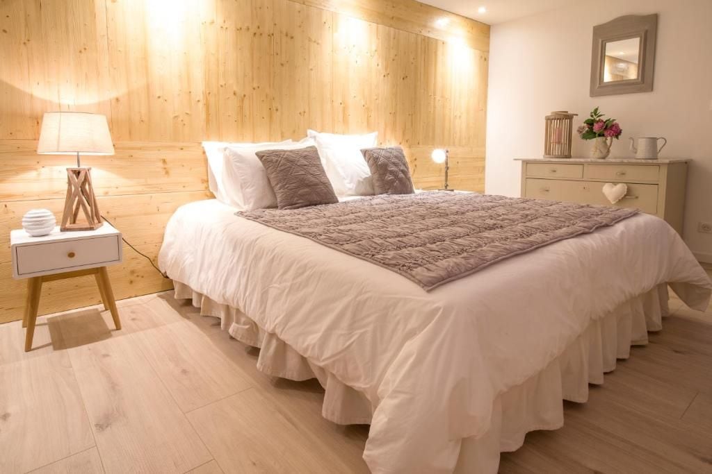 Een slaapkamer met een bed, nachtkastje, lamp, kaptafel en een spiegel aan de muur.