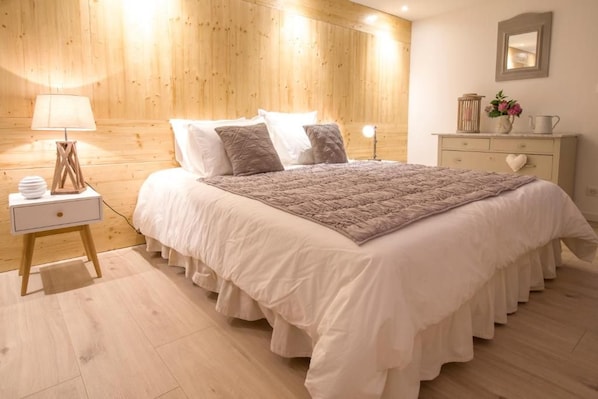 A bedroom with a bed, bedside table, lamp, dresser, and a mirror on the wall.