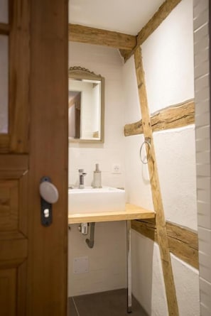 Une salle de bain avec un plafond orné de poutres en bois, un lavabo blanc et un miroir.