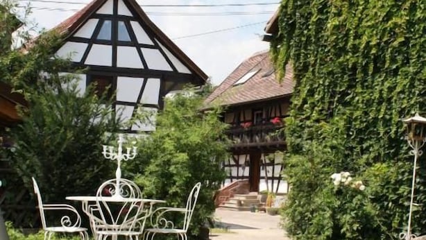 A traditional building with a steeply pitched roof, surrounded by lush greenery. - LA GRANGE AUX COQS (Ittenheim)